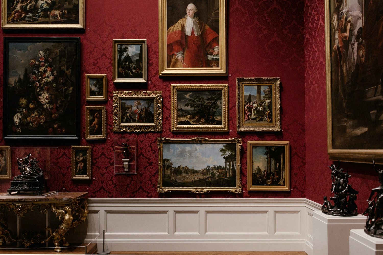 A gallery wall of gilt-framed paintings on red damask