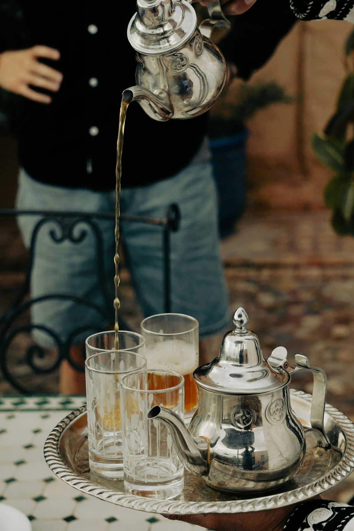 Tea being poured from a silver pot into glasses on a tray